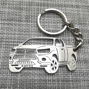 May include: Silver metal keychain featuring a detailed cutout of a pickup truck with the license plate "EX869BP".