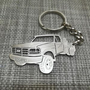 May include: Silver keychain featuring a detailed cutout of a Ford F-350 pickup truck with the text "SCHAEFE2" on the front bumper.
