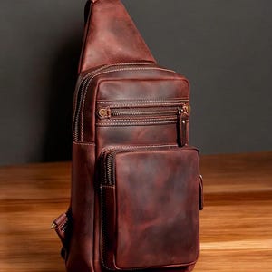 May include: A brown leather crossbody bag with multiple zippered compartments and a flap closure. The bag has a distressed look and is made of high-quality leather.