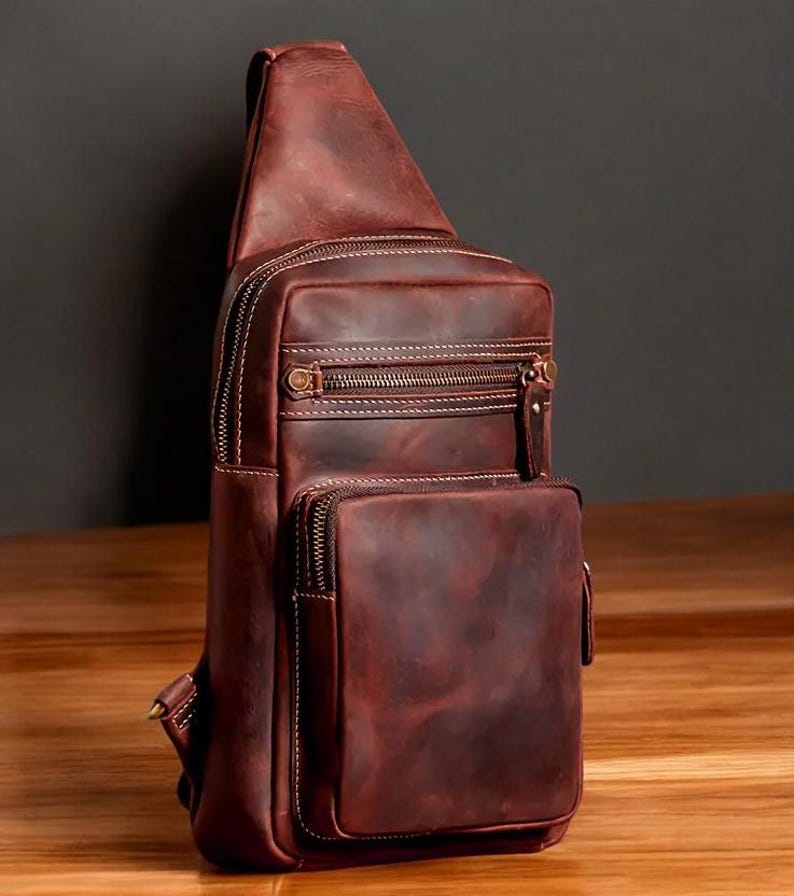 May include: A brown leather crossbody bag with multiple zippered compartments and a flap closure. The bag has a distressed look and is made of high-quality leather.