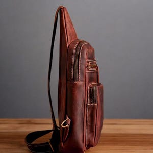 May include: A brown leather crossbody bag with multiple pockets and a zip closure. The bag has a long adjustable strap.