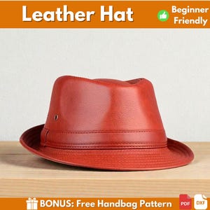 May include: A red leather hat with a fedora style, featuring a structured crown and a wide brim. The hat is displayed on a wooden surface. The text "Leather Hat" is at the top of the image.