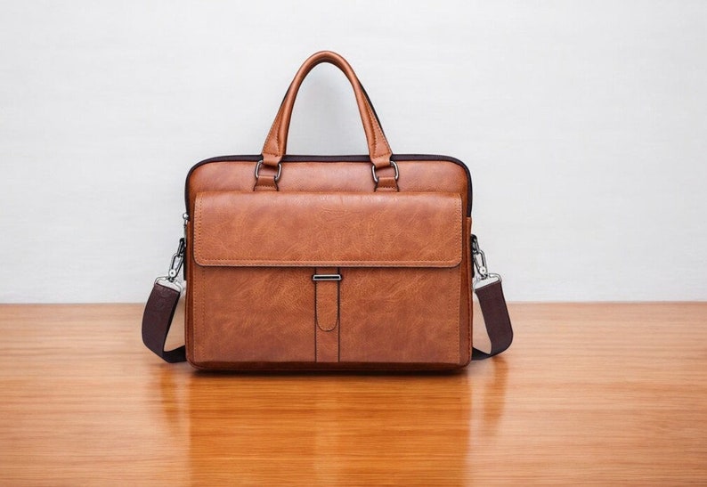 K&ouml;nnte beinhalten: Eine braune Ledertasche mit einer Fronttasche und einem Schultergurt.