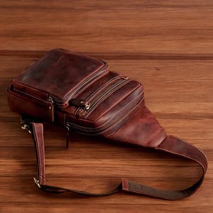May include: A brown leather crossbody bag with multiple zipped compartments and an adjustable strap.