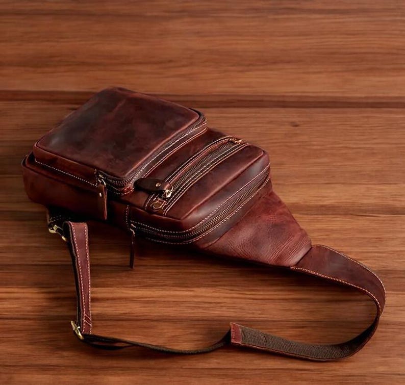 May include: A brown leather crossbody bag with multiple zipped compartments and an adjustable strap.