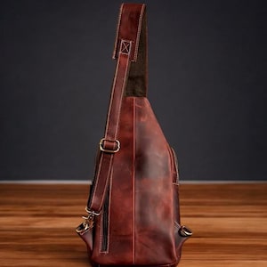 May include: A brown leather crossbody bag with a long adjustable strap. The bag has a flap closure and a zipped pocket on the front.