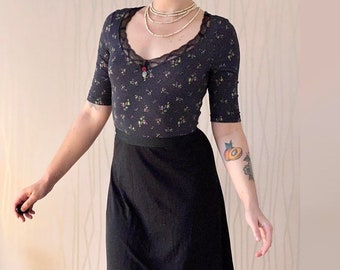 May include: A black skirt with a floral print top. The top has a lace neckline and a small charm hanging from it. The skirt is knee-length and has a simple, A-line silhouette.