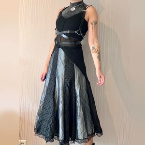 May include: A black and silver skirt with a black leather harness. The skirt has a layered design with a black polka dot pattern and a silver satin-like fabric.