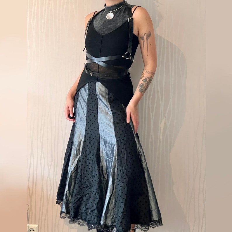 May include: A black and silver skirt with a polka dot pattern and a black leather harness with straps and buckles.