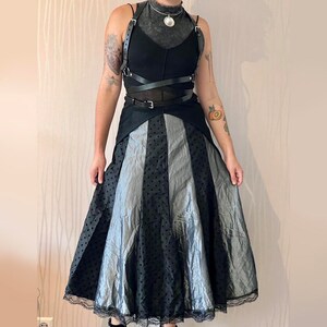 May include: A black and silver polka dot skirt with a black leather harness and a silver pendant necklace.