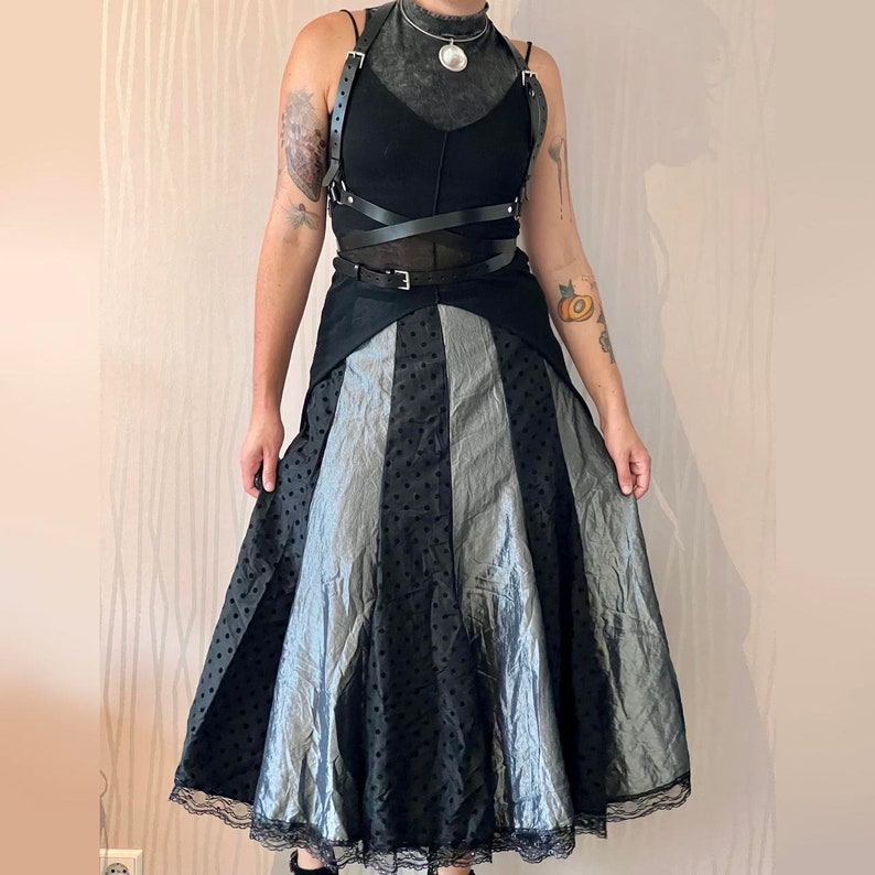 May include: A black and silver polka dot skirt with a black leather harness and a silver pendant necklace.