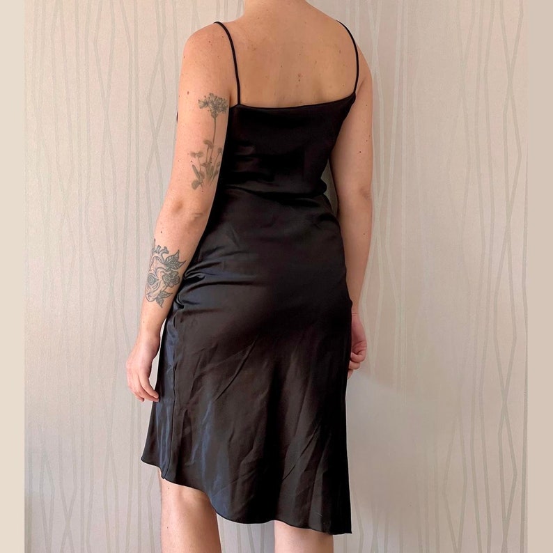 May include: A black satin slip dress with thin straps. The dress has a simple, elegant design and a flowing silhouette.