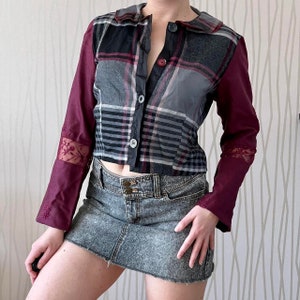 Puede incluir: Una camisa de cuadros burdeos y gris con cuello y mangas largas. La camisa tiene cierre de botones en la parte delantera y una silueta ajustada. La camisa se combina con una minifalda vaquera gris oscuro.