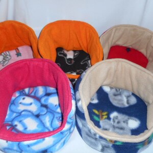 May include: Five small, colorful, fleece-lined pet beds. The beds are in various colors and patterns, including orange, pink, red, blue, and beige. Each bed has a soft, plush lining and a comfortable, rounded shape.