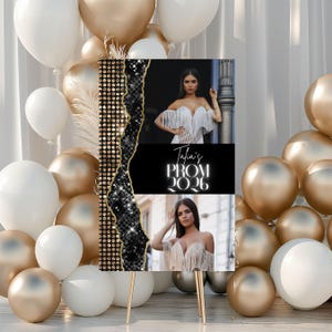 May include: A prom sign featuring two photos of a woman in a white dress, with the text "Talia's PROM 2026." The sign has a black and gold sequined design and is displayed on a gold easel, surrounded by gold and white balloons.
