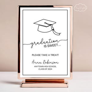 May include: A white sign with a black graduation cap illustration and the text "graduation is sweet..."  The sign also includes the text "Please take a treat!"  "Anna Robinson"  "ANYTOWN HIGH SCHOOL"  "CLASS OF 2024". The sign is on a gold stand.