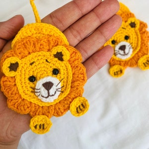 Puede incluir: Dos adornos de león de crochet hechos con hilo amarillo y naranja. Los leones tienen ojos marrones, narices blancas y bigotes marrones. Tienen una melena de crochet marrón y una pequeña cola naranja.