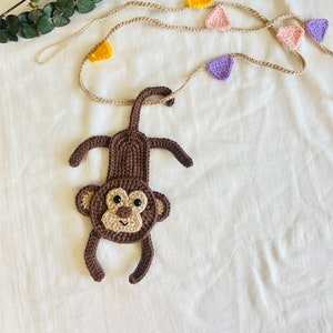May include: A brown crocheted monkey hanging from a string of colorful crocheted triangles. The triangles are yellow, pink, and purple.
