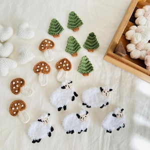 Può includere: Una collezione di oggetti all'uncinetto tra cui alberi, funghi, cuori e pecore. Gli oggetti sono bianchi, verdi e marroni.