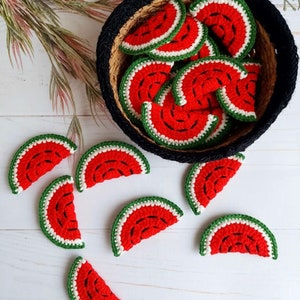 Puede incluir: Posavasos artesanales con forma de rodajas de sandía. Los posavasos rojos tienen detalles de semillas negras, ribetes blancos y bordes verdes de ganchillo. Algunos están en una cesta negra tejida, otros sobre una superficie de madera blanca.