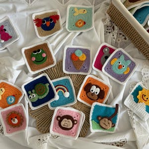 Peut inclure: Une collection de 12 carrés au crochet colorés présentant différents motifs sur le thème des animaux et de la nature. Chaque carré a une bordure blanche et est décoré de différentes couleurs et textures.