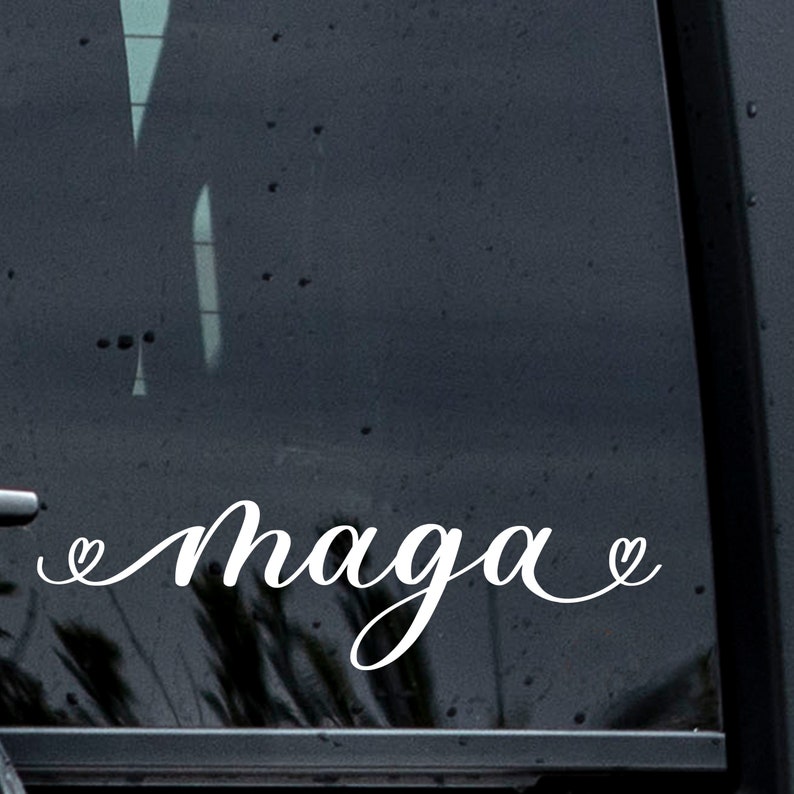 May include: A white vinyl sticker with the text "Maga" in cursive lettering with a heart symbol on each side of the text.