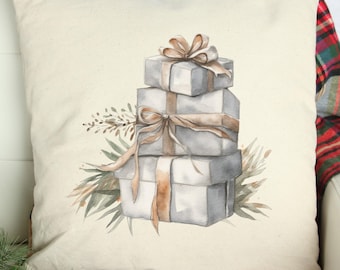 May include: A square, off-white pillow with a watercolor illustration of three stacked, gray gift boxes tied with tan ribbons. Green and brown foliage surrounds the gifts, creating a festive, holiday theme.
