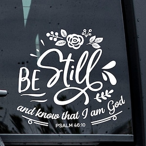 May include: White vinyl decal with the words "BE Still and know that I am God" in a decorative script font. Floral and leaf accents are above the word "Still". The text "PSALM 46:10" is below the main text.