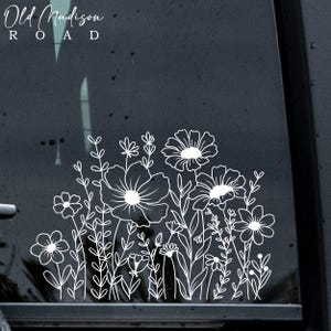 May include: White outline floral design on a dark gray background. The design features a variety of flowers and leaves, including daisies, poppies, and ferns. The text "Old Madison Road" is at the top of the image.