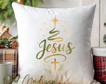 May include: White square pillow with a Christmas tree design. The design features the word "Jesus" in a script font, a cross, and a star. The tree is green and gold, with gold stars. The pillow has the text "Old Madison Road" at the bottom.