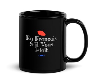 May include: Black ceramic coffee mug with a white design that says "En Francais S'il Vous Plait" with a red beret and a blue mustache.