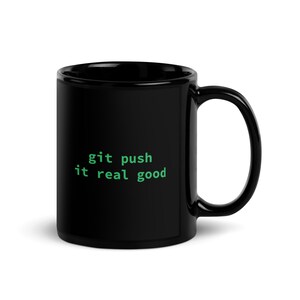 Può includere: Tazza da caffè nera con un design di testo verde che dice "git push it real good".