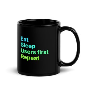 Puede incluir: Taza de café negra con un diseño blanco que dice "Eat Sleep Users first Repeat" en un degradado de azul y verde.