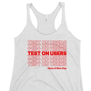 Può includere: Canotta grigio chiaro con le parole "TEST ON USERS" in rosso ripetute più volte. La frase "Have A Nice Day" è stampata in rosso nella parte inferiore della canotta.