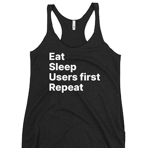 Może przedstawiać: Czarny top na ramiączkach z białym napisem "Eat Sleep Users first Repeat". Top ma okrągły dekolt i krój bokserki. Tkanina wydaje się być miękkim, melanżowym materiałem.