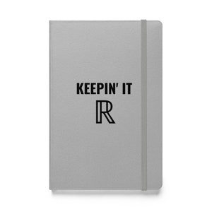 May include: A gray notebook with the text "KEEPING IT R" printed in black. The notebook has a matching gray elastic band closure and a minimalist design. The cover is smooth and the overall aesthetic is modern and clean.