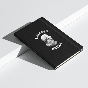 May include: Black notebook with a white graphic of a man's profile and the text "LAISSEZ FAIRE" in a circle.