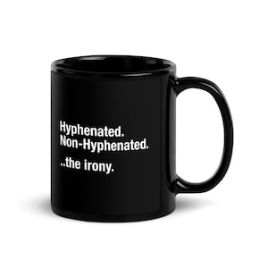 Puede incluir: Taza de cerámica negra con texto blanco: "Hyphenated. Non-Hyphenated. ..the irony." La taza tiene un asa grande y un acabado brillante. Un diseño simple pero humorístico.