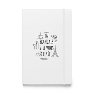 May include: White notebook with the phrase "En Francais S'il Vous Plait" and illustrations of French icons like a croissant, Eiffel Tower, and wine bottle. The notebook has a vertical elastic band closure.
