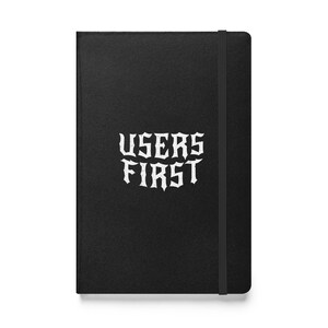 Może przedstawiać: Czarny notes, oprawiony w skórę, z białym napisem "USERS FIRST" w stylu gotyckim.