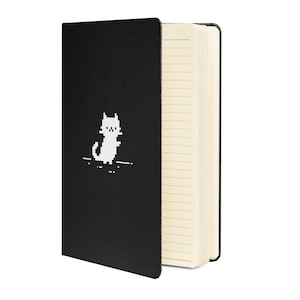 May include: Black notebook with a white pixelated cat design on the front cover. The notebook has lined pages.