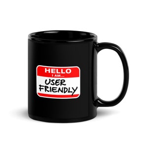 Könnte beinhalten: Schwarze Keramik-Kaffeetasse mit einem roten und weißen Namensschild, auf dem "Hallo, ich bin... Benutzerfreundlich" steht.