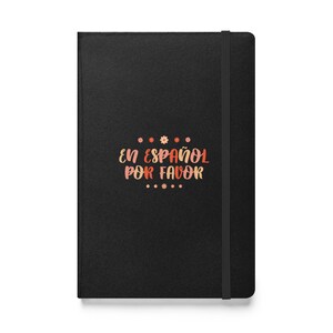 May include: Black notebook with a black elastic closure. The front cover features the text "EN ESPAÑOL POR FAVOR" in pink and orange lettering with small flower accents.