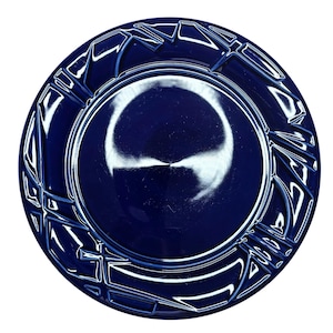 May include: A round, navy blue plate with a glossy finish. The plate features a raised geometric pattern around the rim, adding a decorative element. The center of the plate is smooth and reflects light.