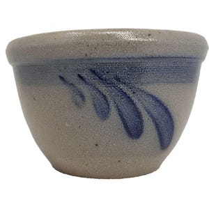 Puede incluir: Un pequeño cuenco de gres con una base gris claro y un diseño de hoja azul estilizado. El cuenco tiene una forma redondeada con un borde ligeramente ensanchado. El diseño azul está pintado en el lateral del cuenco.