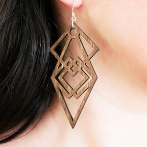 Peut inclure: Une paire de boucles d'oreilles en bois avec un motif géométrique. Les boucles d'oreilles sont brunes et ont une forme de diamant avec un plus petit diamant à l'intérieur.