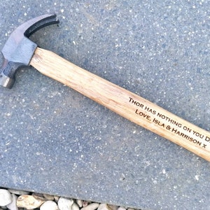 May include: A wooden handled hammer with a black metal head. The handle is engraved with the message "Thor has nothing on you Dad! Love, Isla & Harrison x".