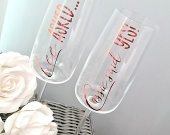 May include: Two champagne flutes with gold lettering. One flute says "He asked..." and the other says "...and she said yes!"