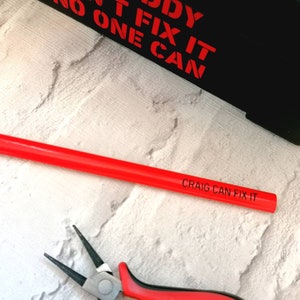 Może przedstawiać: Czerwony ołówek z napisem "CRAIG CAN FIX IT". Na zdjęciu widoczne są również szczypce.