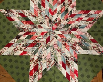 May include: A handmade Christmas star quilt with a green background and a large star in the center. The star is made of various patterned fabrics in red, white, and green. The background has a repeating snowflake pattern.